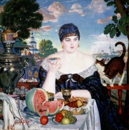 Борис Кустодиев, «Купчиха, пьющая чай». Статная румяная женщина сидит за богато накрытым столом с самоваром и фруктами на фоне живописного провинциального города